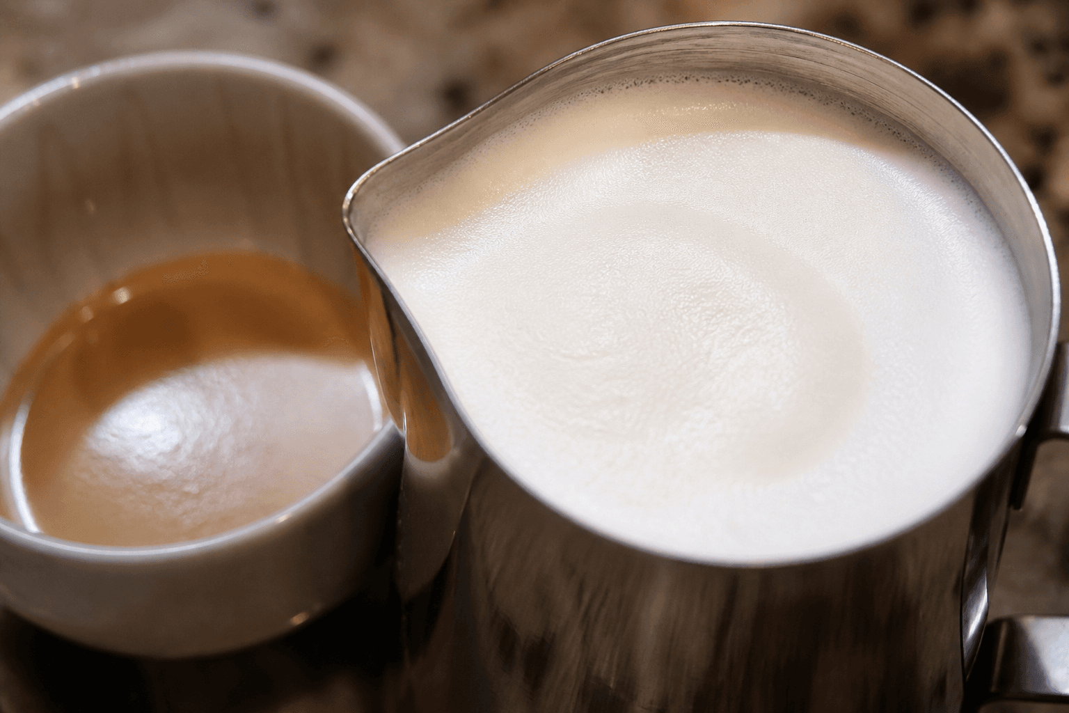 Blankt mælkeskum i kande ved siden af kaffekop