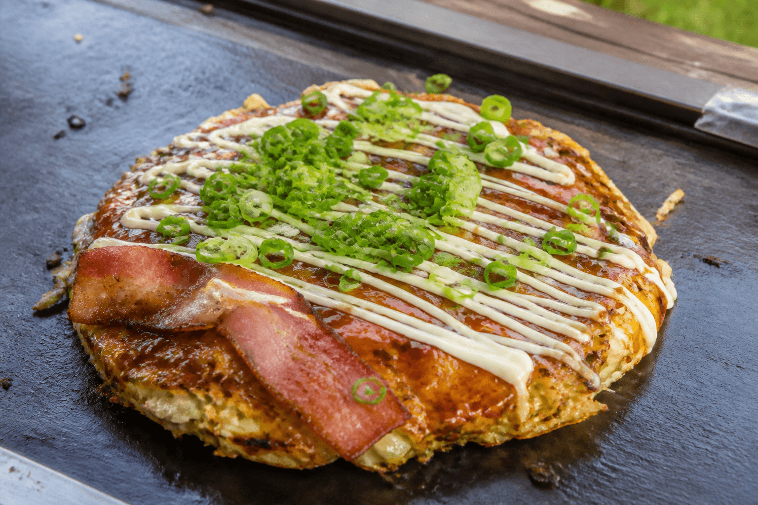 Japansk okonomiyaki på plancha med sauce, mayonnaise og forårsløg